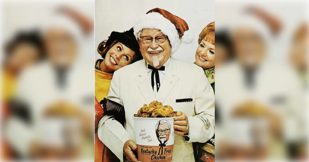 KFC Colonel Sanders in a Santa hat holding a Kentucky Fried Chicken bucket