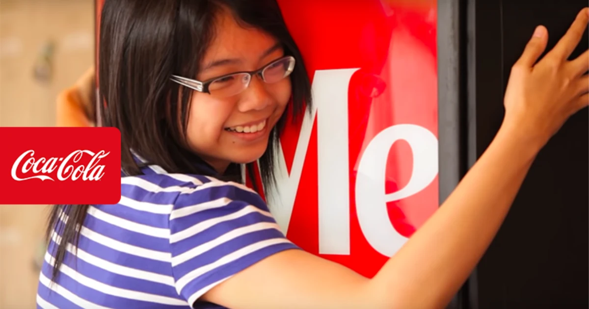 Smiling girl in glasses hugging a red Coca-Cola Hug Me machine