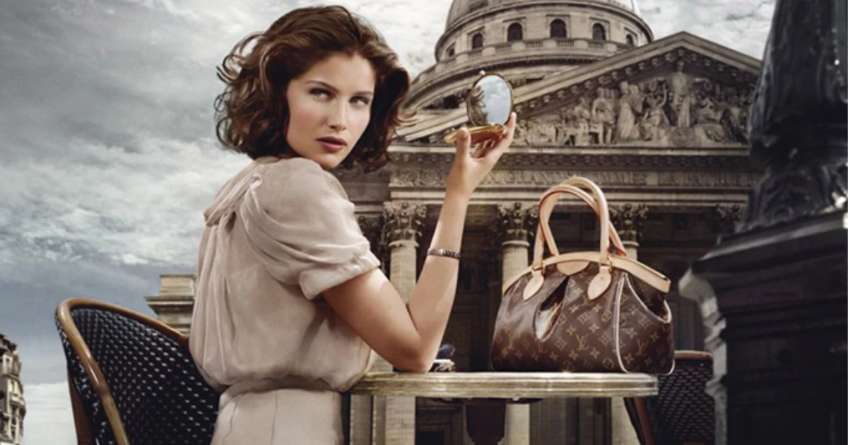 A Louis Vuitton advertisement for the Tivoli, cut in 2014 — Louis Vuitton A dark-haired model at a Paris café table holding a compact mirror, a Louis Vuitton Monogram Tivoli beside her with the Panthéon behind