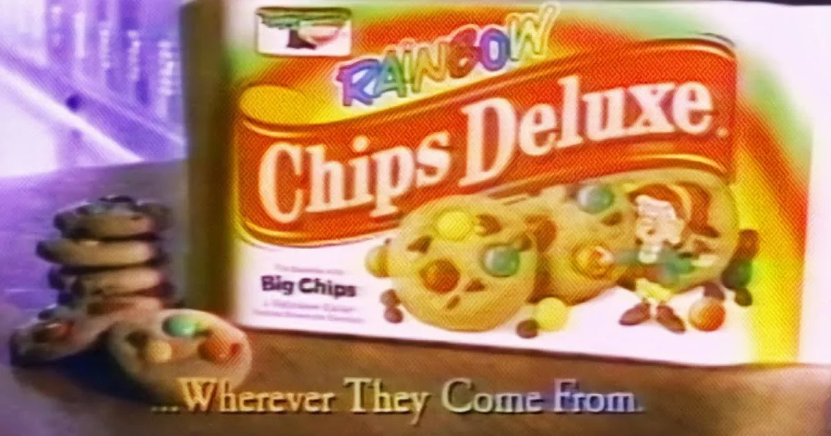 A frame from an early Rainbow Chips Deluxe TV spot—“…Wherever They Come From” — Keebler Rainbow Chips Deluxe box with candy-coated chocolate chips in a late-1980s Keebler TV commercial