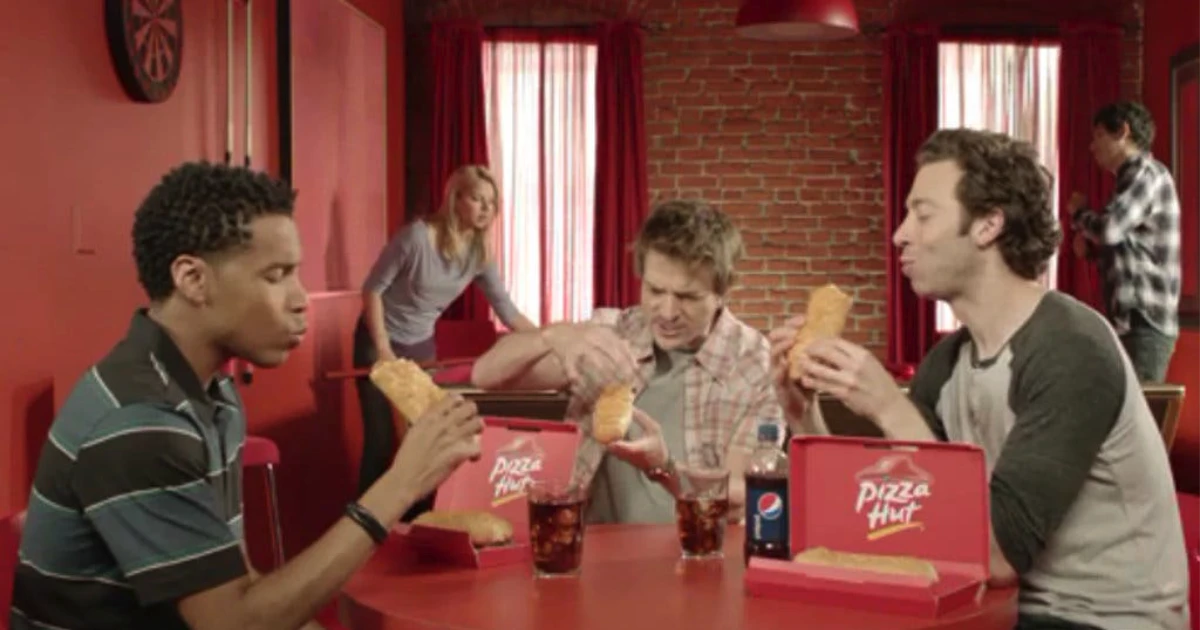 Pizza Hut Four men eating Pizza Hut P'Zolo rolled sandwiches at a red table