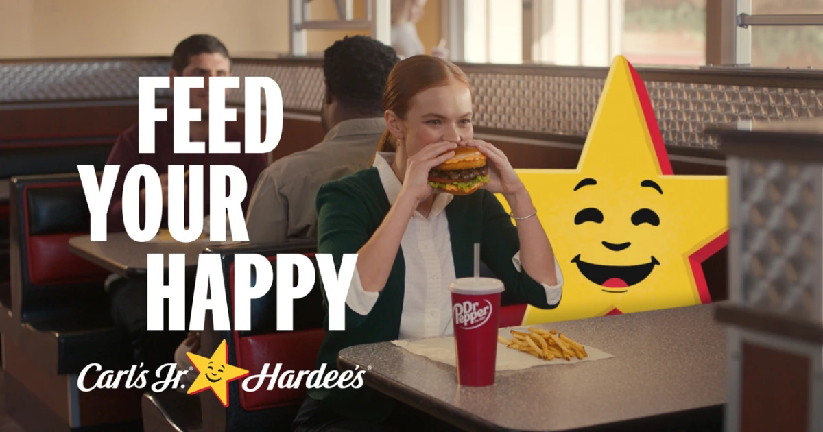 The Happy Star in a joint Carl's Jr. and Hardee's campaign — Carl's Jr./Hardee's The Happy Star mascot seated in a booth beside a customer in a Carl's Jr. and Hardee's “Feed Your Happy” ad