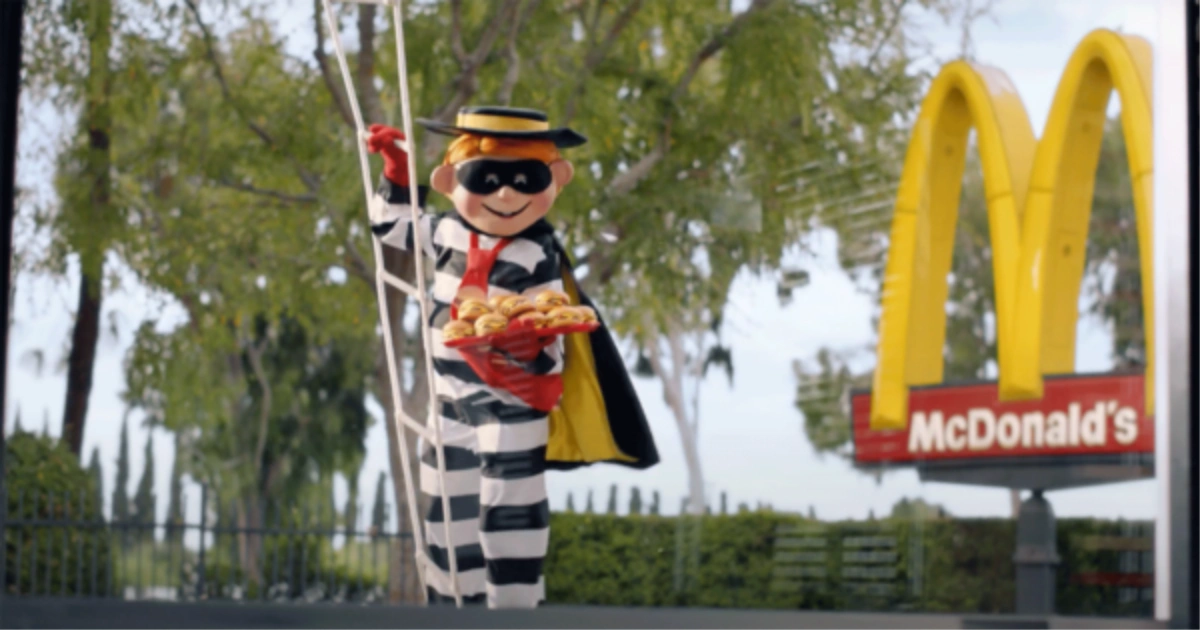 The Hamburglar mascot in striped outfit and mask holding a tray of hamburgers