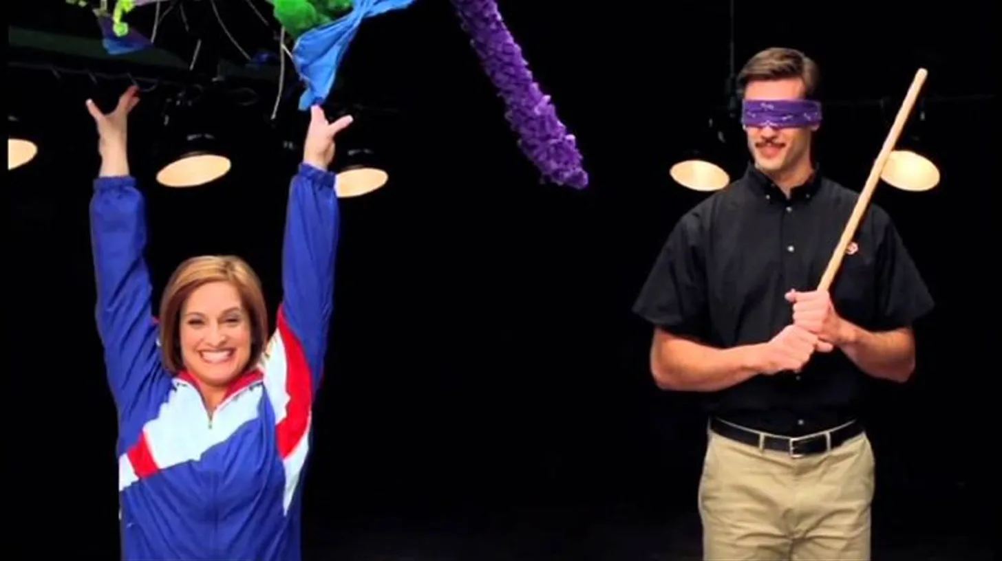 Mary Lou Retton emerges from the piñata in the RiDQulous campaign / Dairy Queen Mary Lou Retton raising her arms beside a blindfolded pitchman holding a piñata stick in a Dairy Queen ad