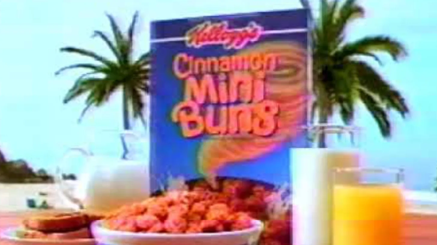 Kellogg's Cinnamon Mini Buns cereal box and a bowl of the swirled pieces on a beach breakfast table with palm trees in a 1990s TV commercial
