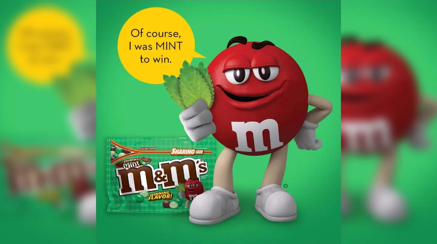 Red celebrates Crunchy Mint, the 2018 Flavor Vote winner, in an M&M’s ad — Mars, Inc. Red M&M character holding mint leaves beside a Sharing Size bag of Crunchy Mint M&M’s marked Winning Flavor