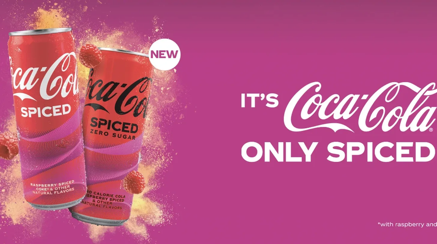 Coca-Cola Spiced and Spiced Zero Sugar cans with raspberries on the pink launch artwork